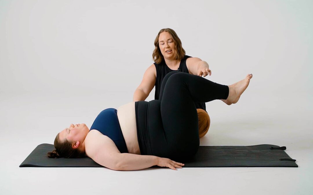 Jessie is seated on the ground, performing a diastasis recti assessment, to check the healing on a woman who is laying on her back with her legs in "tabletop" position.