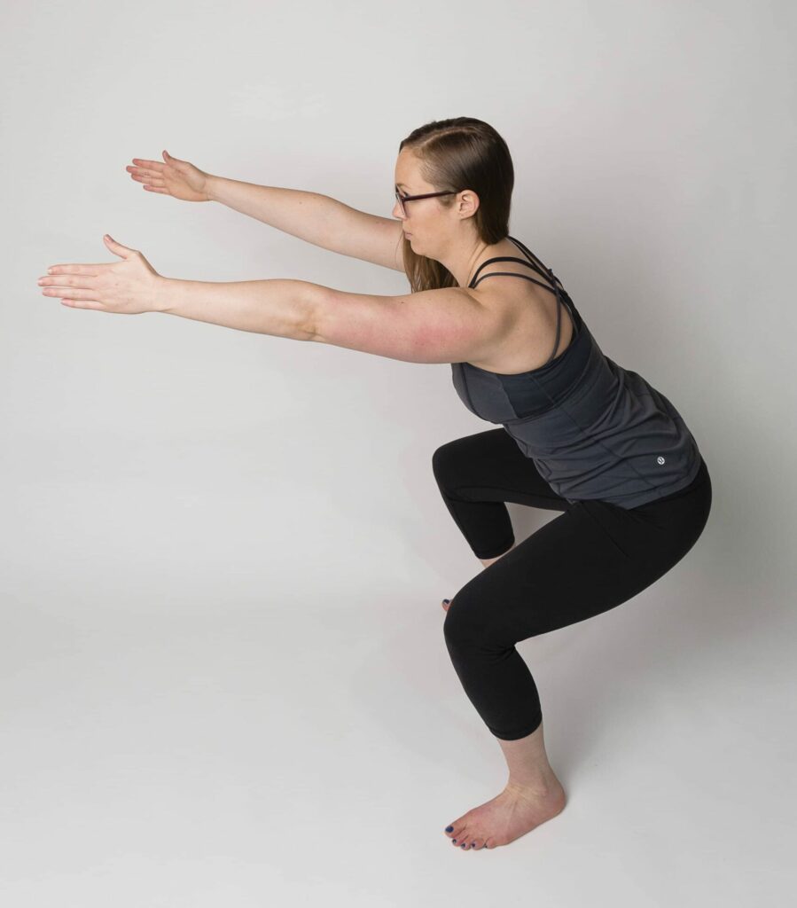 A woman in a squat position, with her arms extended out and slightly above shoulder height, is demonstrating an exercise that might be done after c-section.